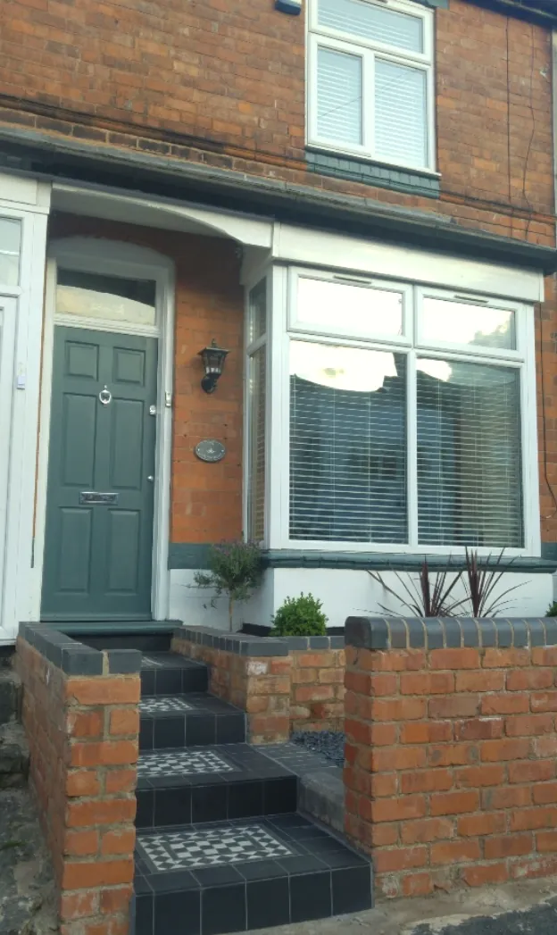 A sage-green front door with Victorian tiled steps — the welcome